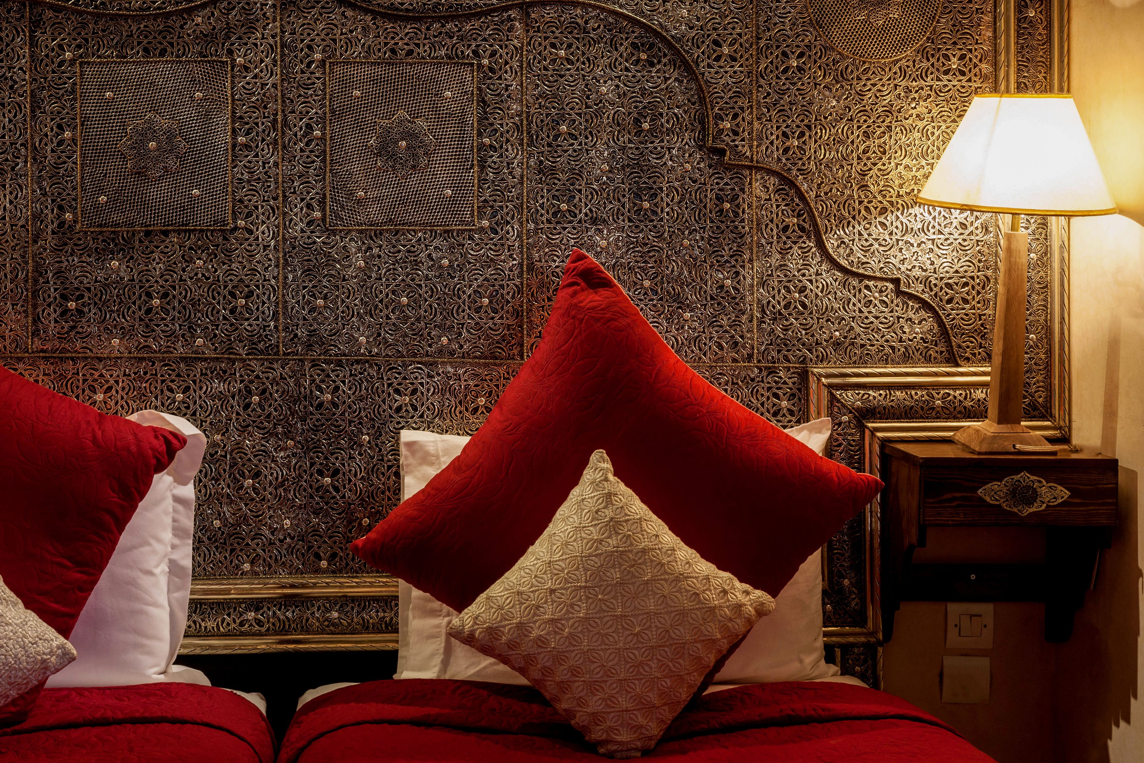 A bed with red and white pillows, a lamp, and an intricately designed headboard.