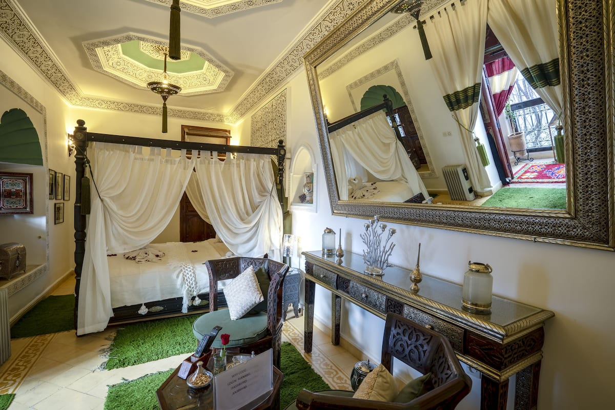 A traditional room with a four-poster bed, a large ornate mirror, and a green carpet.