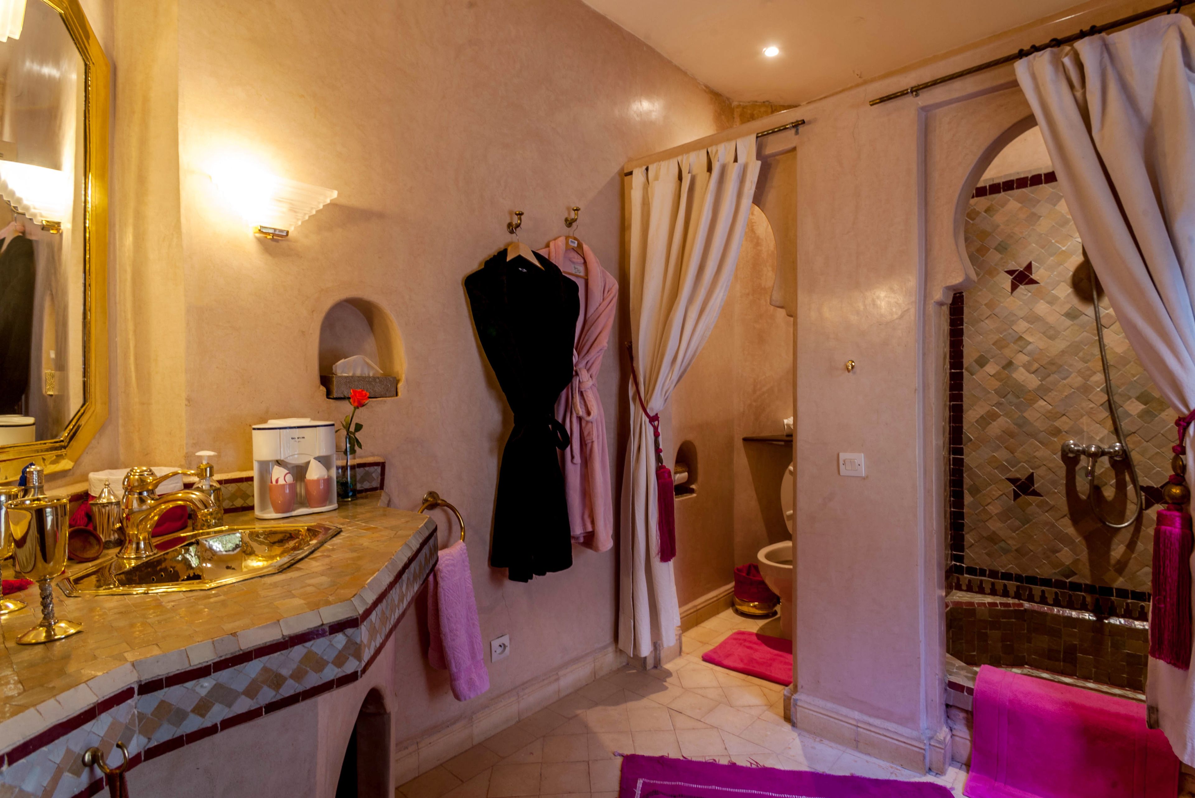 A bathroom with a large mirror, a sink with gold fixtures, a shower with a glass door, and a tiled floor.