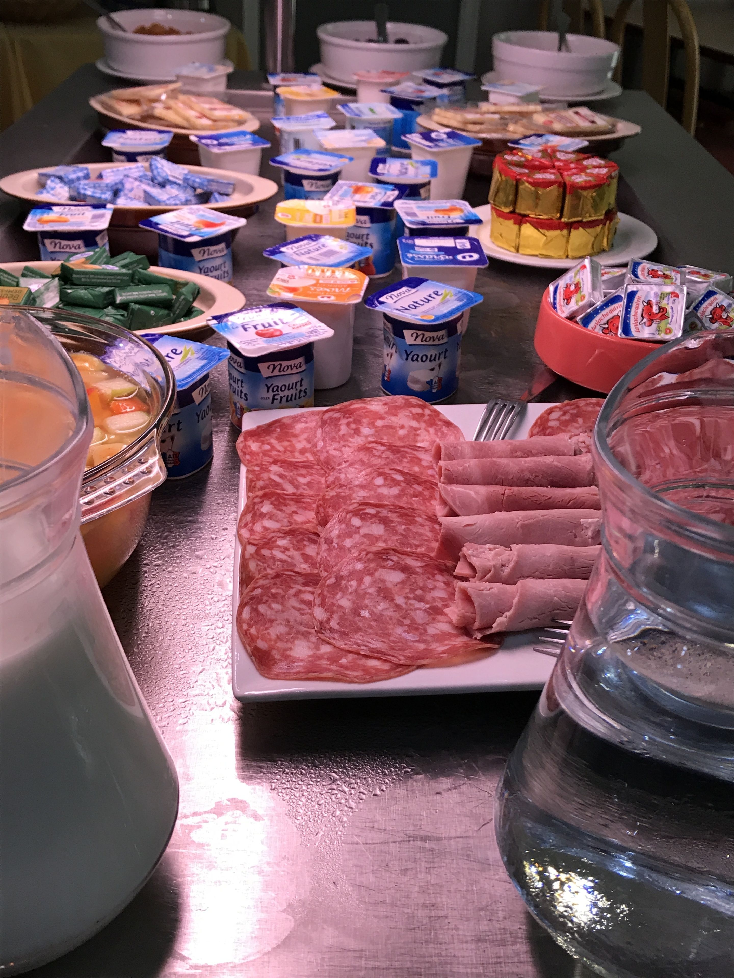 Una mesa de buffet con diversos alimentos, como carnes en rodajas, queso y recipientes de yogur.