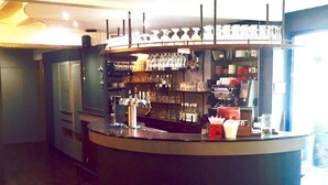 Una zona de bar con estantes llenos de vasos y botellas, una barra con una caja registradora y vistas al exterior a través de una ventana.