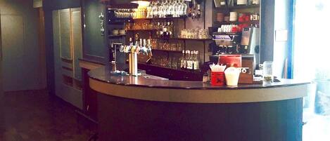 A bar area with shelves of glasses and bottles, a counter with a cash register, and a view of the outside through a window.