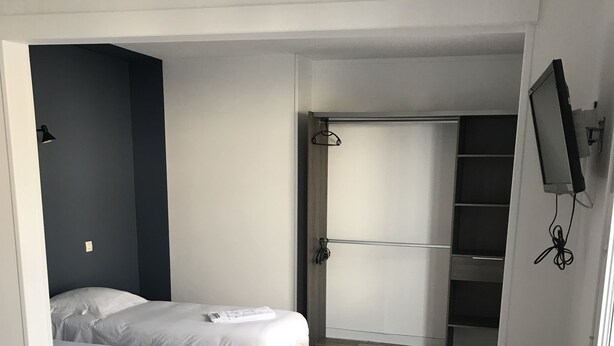 Habitación de hotel pequeña con dos camas, suelo de madera, televisor montado en la pared y un escritorio pequeño.