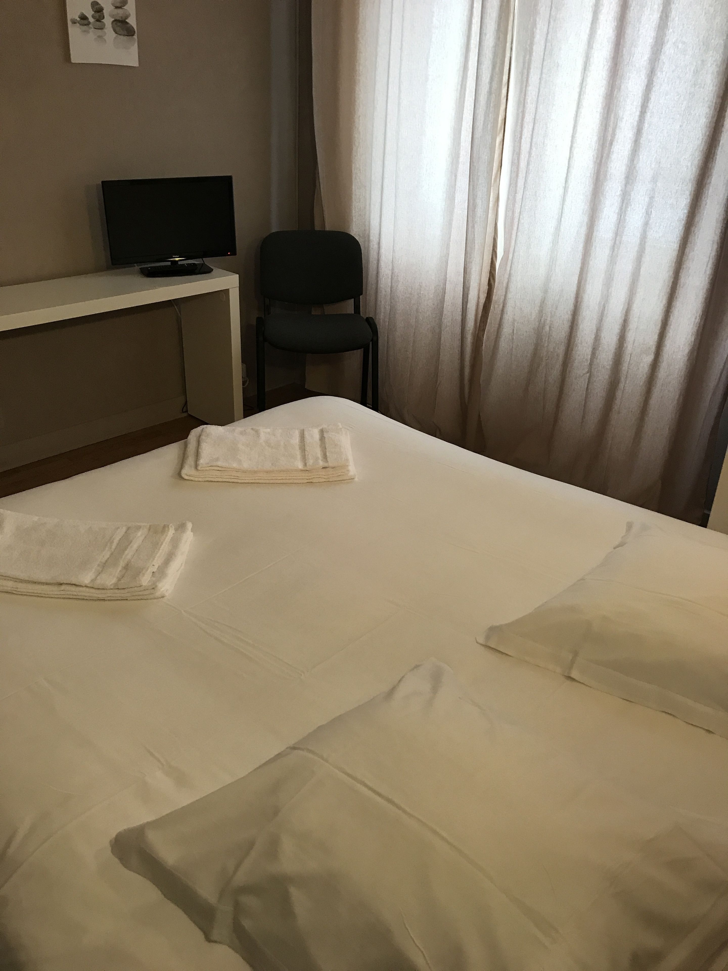 A hotel room with a bed, a desk with a computer, and a chair.