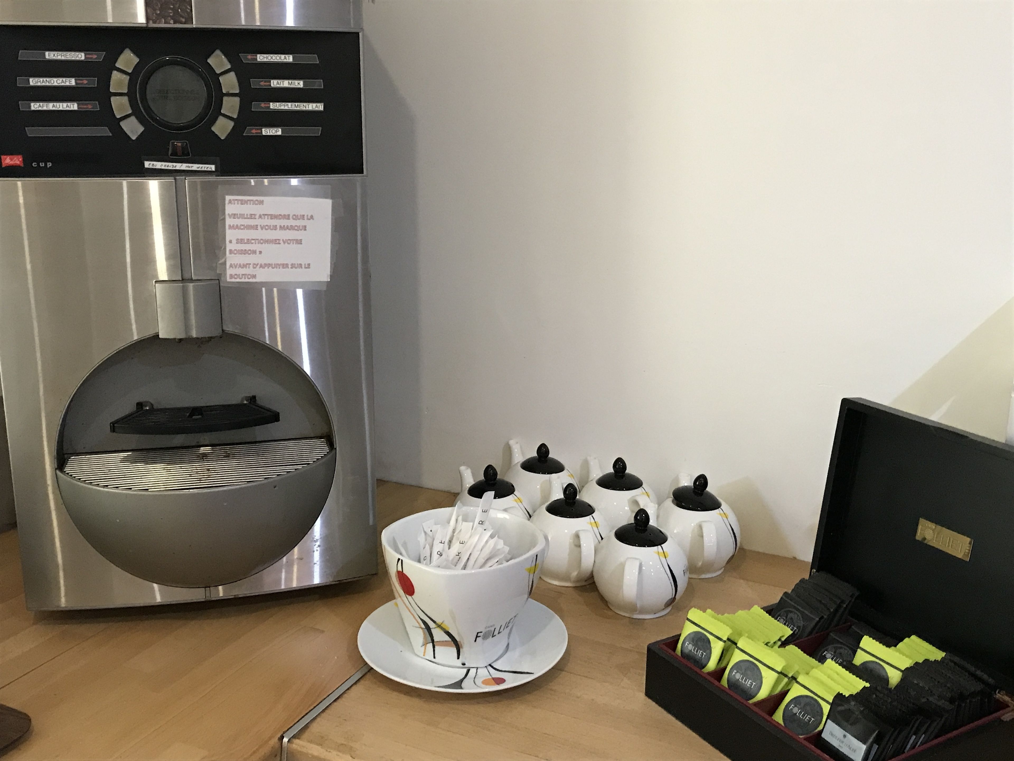A coffee machine with various drink options, a cup of coffee, several teapots, and a box of coffee pods.