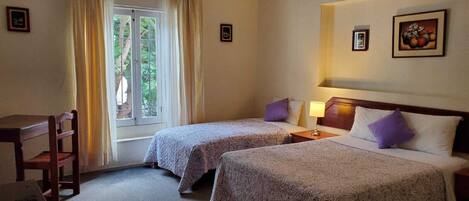 Ett hotellrum med två sängar, ett skrivbord och ett fönster med gardiner.