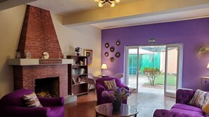 A living room with a brick fireplace, purple sofas, a coffee table, and a bookshelf. - Hostal The Place Miraflores (Lima)