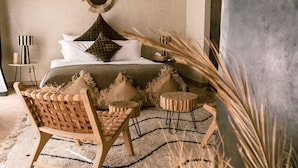 A bedroom with a bed, two nightstands, a round mirror, and a woven chair.