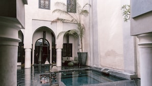 A courtyard with a pool, columns, arches, and a seating area.