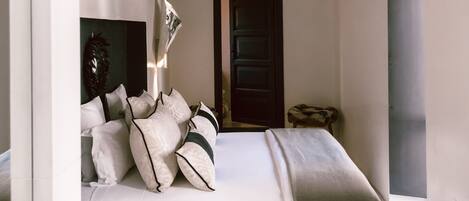 A bedroom with a bed, a small round table, a hanging light fixture, and a door.
