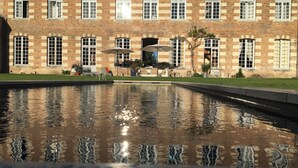 Un edificio con fachada de ladrillo, múltiples ventanas y una fuente reflectante al frente.