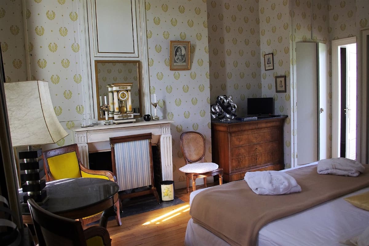 Una habitación de hotel con cama, escritorio con lámpara, una silla, radiador y armario.