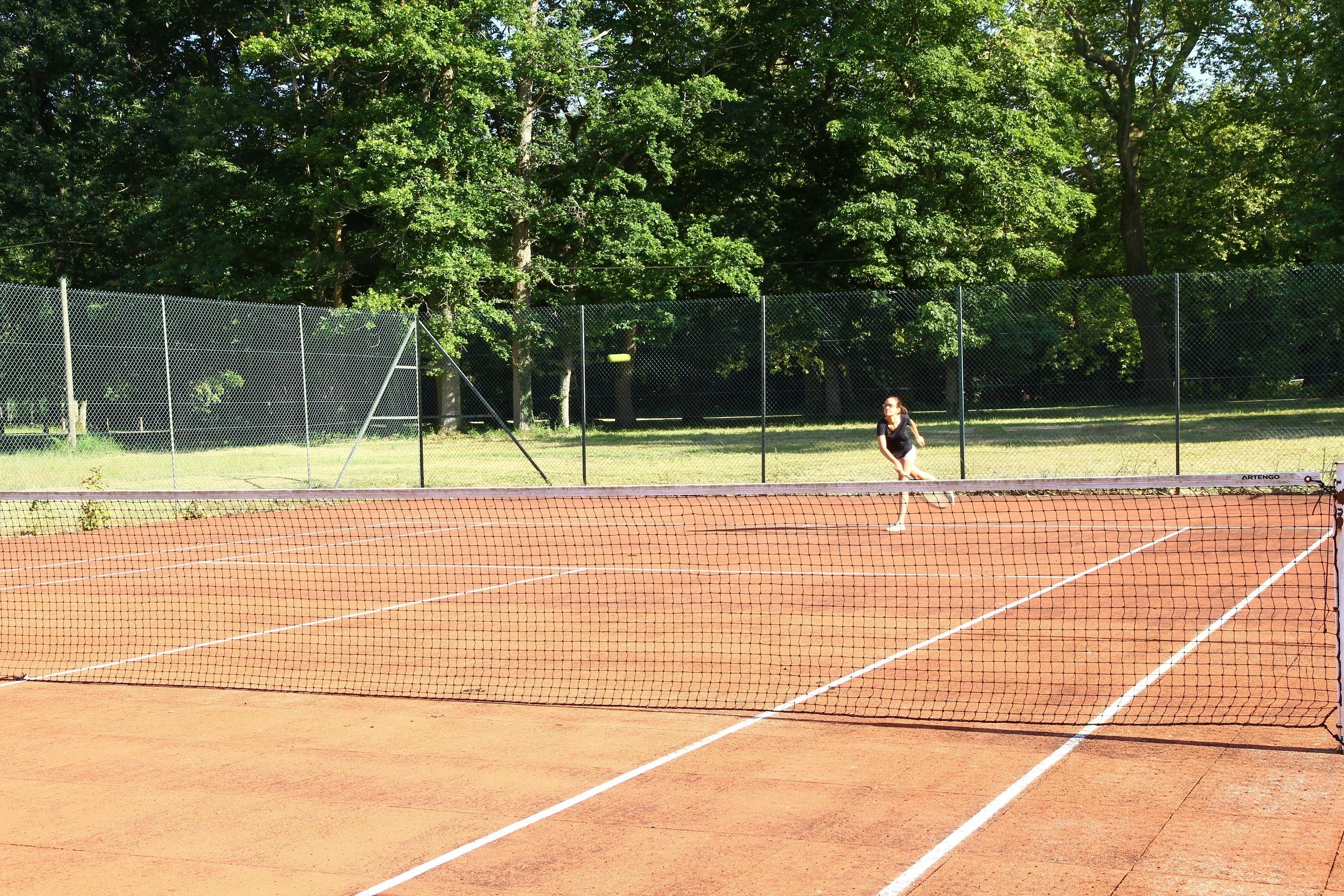 A tennis court with a net, surrounded by a fence and trees.