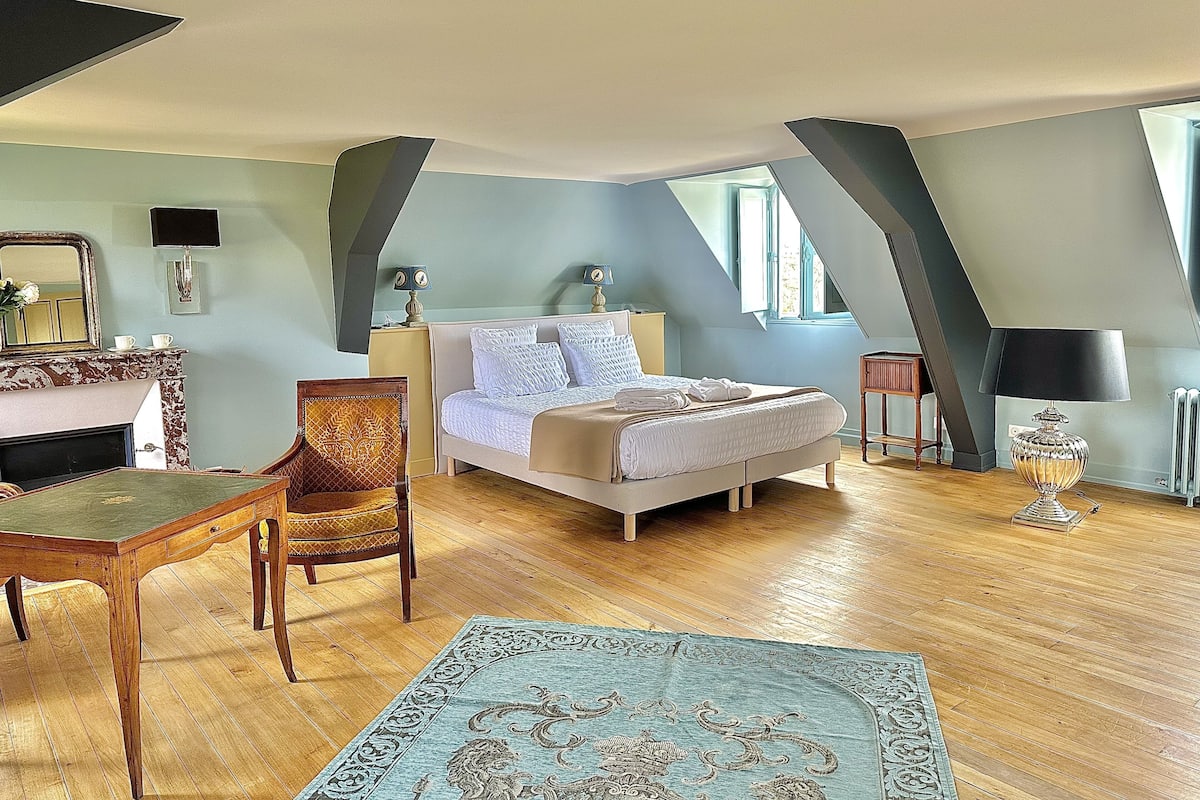 Un dormitorio con una cama, una silla, una mesa, una lámpara y un espejo.