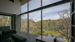 A modern interior with large windows, a stone floor, and a view of a mountain and trees. - Zaborin (Kutchan)