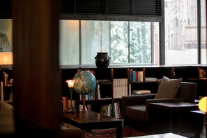 A cozy reading area with a globe lamp, bookshelves, and a comfortable chair by a window with a view of trees.