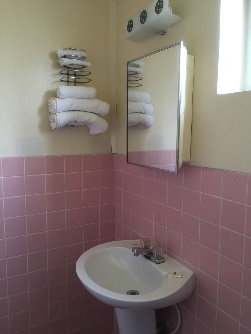 Un baño con azulejos rosas, un lavabo blanco y un espejo con toallas colgadas en un perchero.