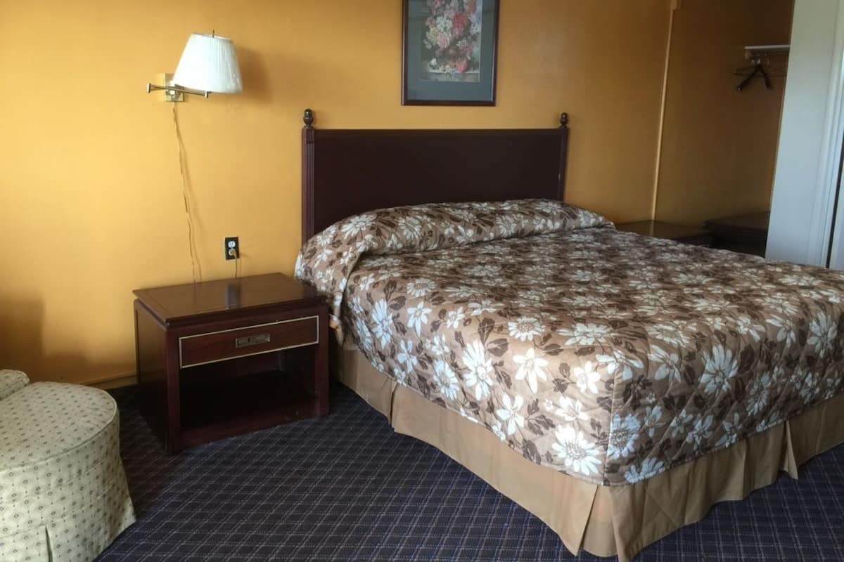 Quarto de hotel com uma cama, mesa de cabeceira, abajur, quadro na parede e uma porta.