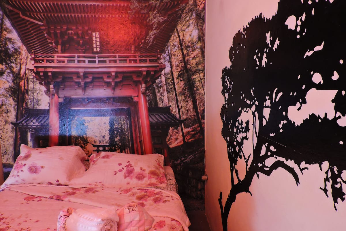 A bed with floral bedding and a rolled towel, a wall with a black tree decal, and a traditional architectural ceiling.
