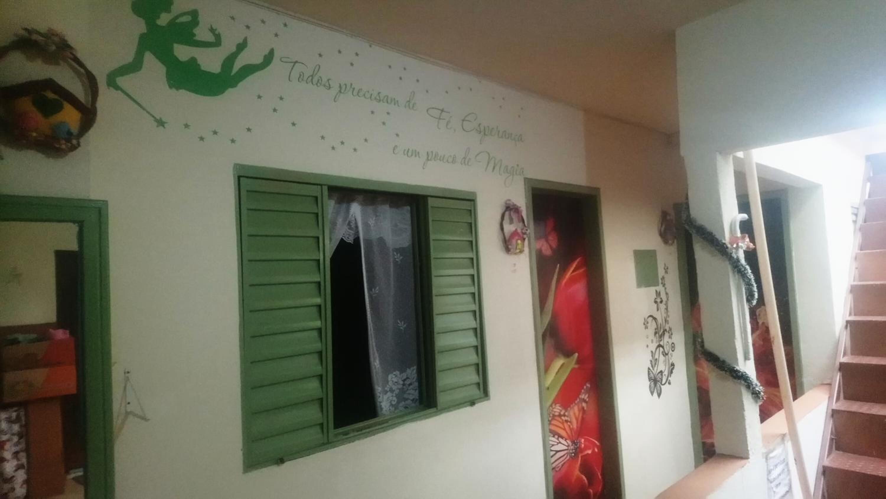 Ein Zimmer mit Fenster, versehen mit grünen Fensterläden, einer Wand mit Wandgemälde und einer Treppe, die zu einer weiteren Ebene führt.