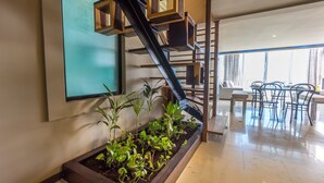 Een modern interieur met een houten trap, een eethoek met metalen stoelen en een plantenbak met groene planten.