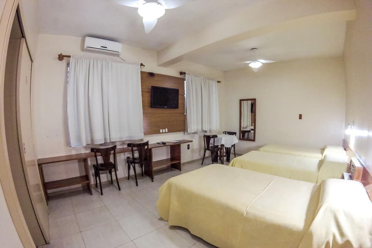 A hotel room with a desk, two beds, a mirror, and an air conditioning unit.