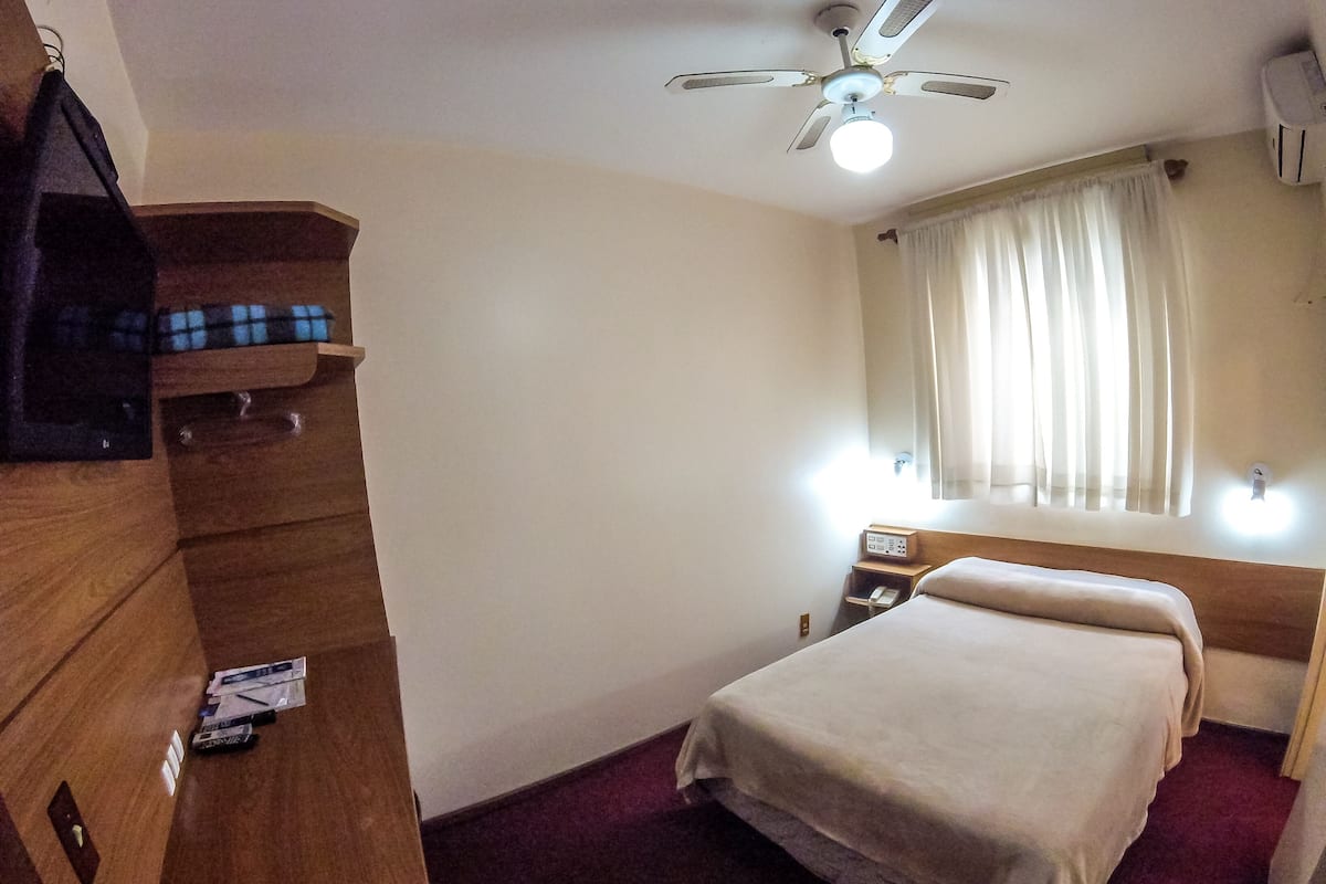 A hotel room with a bed, a wooden wardrobe, a ceiling fan, and a window with curtains.