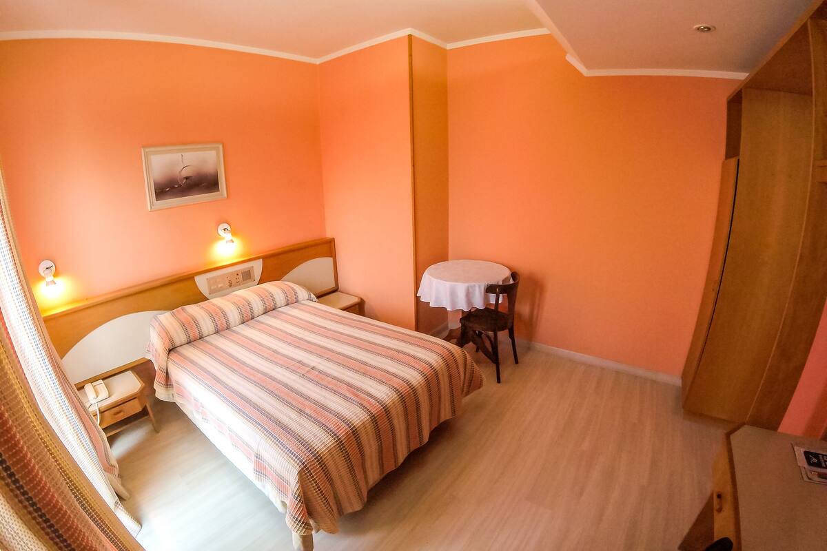 A bedroom with a bed, bedside tables, a small table with a chair, and a door.