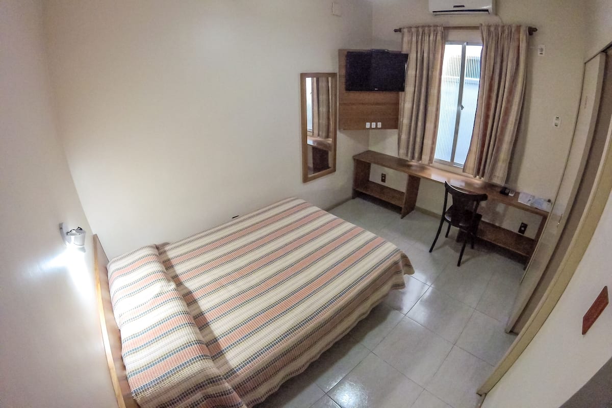 A bedroom with a bed, a desk, a chair, a ceiling fan, and an air conditioning unit.