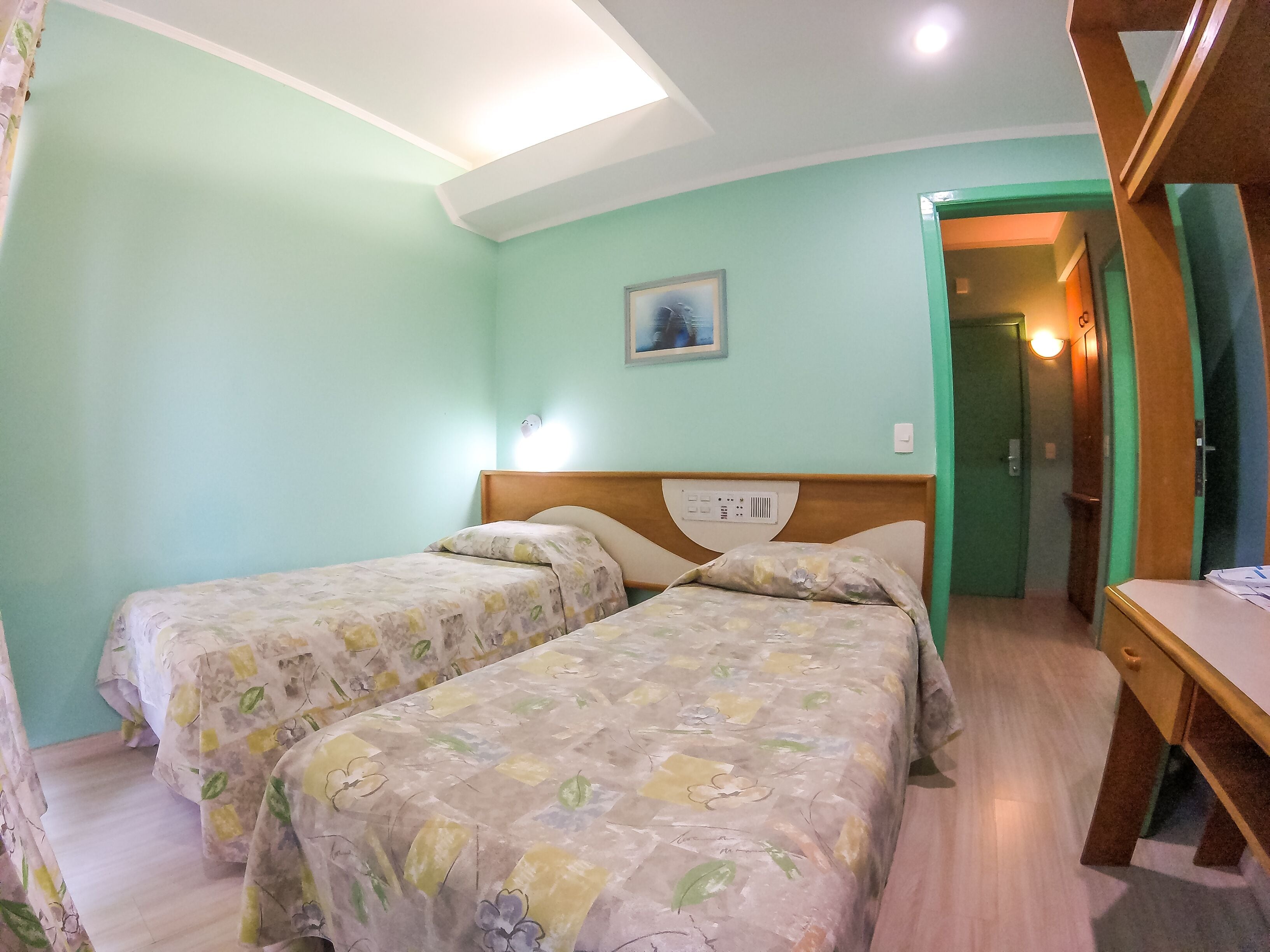 A room with two beds, a wooden headboard, a nightstand, and a painting on the wall.