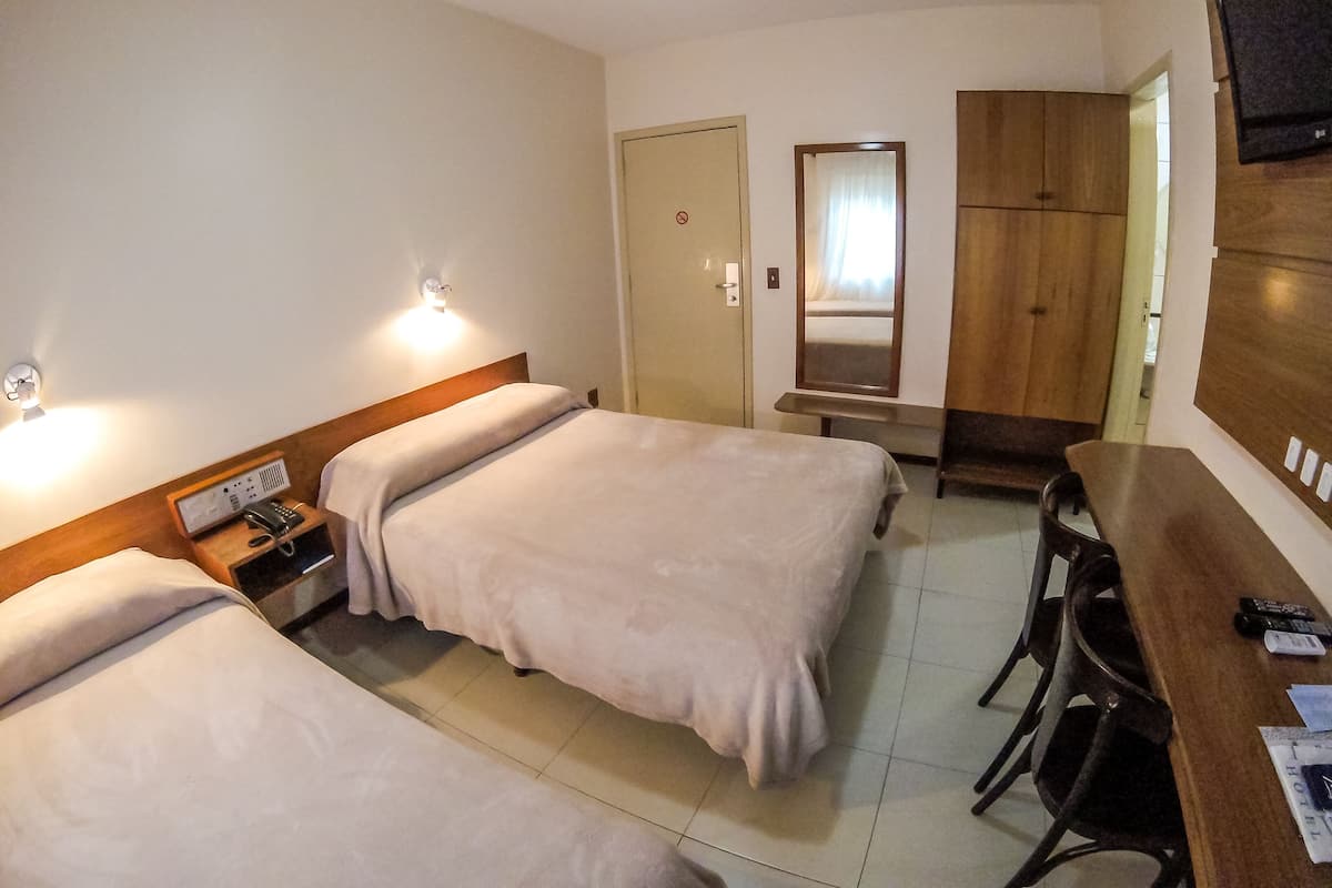 A hotel room with two beds, a desk, a chair, a TV, and a wardrobe.