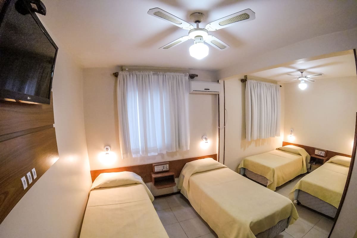 A hotel room with two single beds, a ceiling fan, a TV, and a mirror.