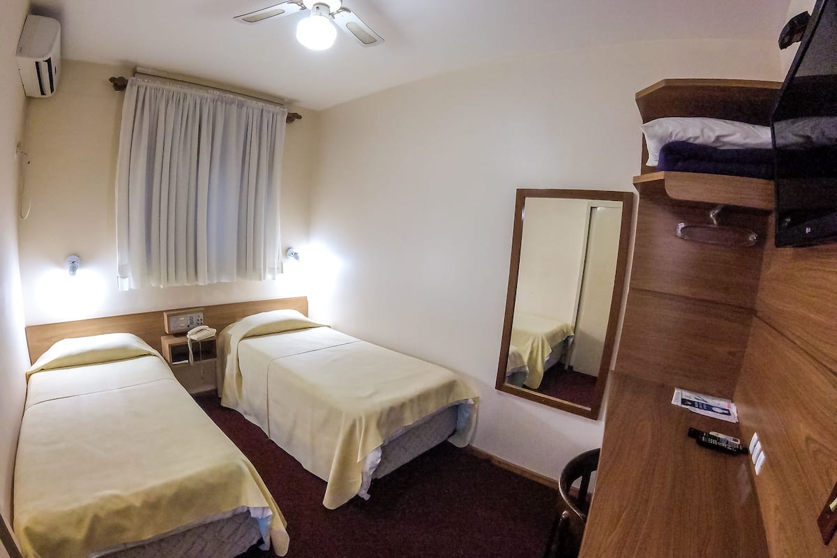 A hotel room with two single beds, a wooden dresser, a mirror, a bedside table with a lamp, and a ceiling fan.