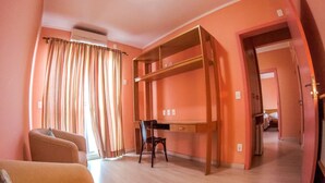 Una habitación con sofá, escritorio y silla, cama individual superior e inferior, y ventana con cortinas.