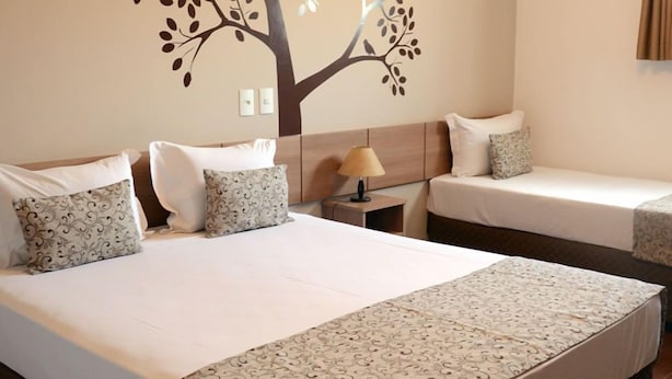 A hotel room with two beds, a nightstand, a lamp, and a wall decoration of a tree. - Pousada Vitalis (Olímpia)
