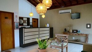 A reception area with a wooden desk, a potted plant, and a television on the wall. - Pousada Vitalis (Olímpia)