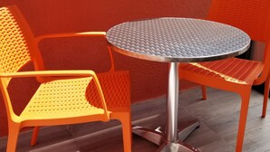 Una mesa redonda con base metálica, rodeada por dos sillas naranjas con respaldo de malla.