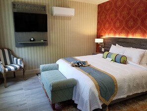 A hotel room with a large bed, a television mounted on the wall, a striped armchair, and a bench. - Sens Hotel & Vanne Bistro Berkeley (Berkeley)