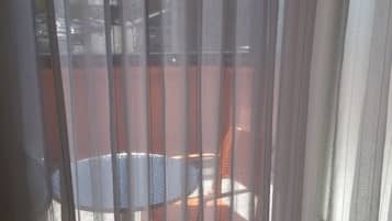 Una vista a través de cortinas traslúcidas, mostrando una mesa redonda y sillas en el exterior, con un edificio y automóviles estacionados al fondo.