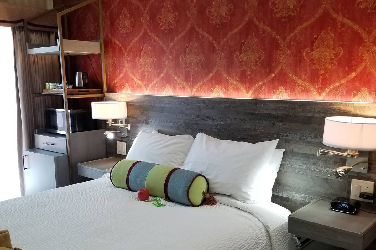 Habitación de hotel con una cama grande, dos mesitas de noche, un armario y un papel tapiz estampado.