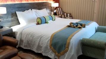 A hotel room with a large bed, a headboard, a desk with a lamp, a chair, a small table, and a striped curtain.