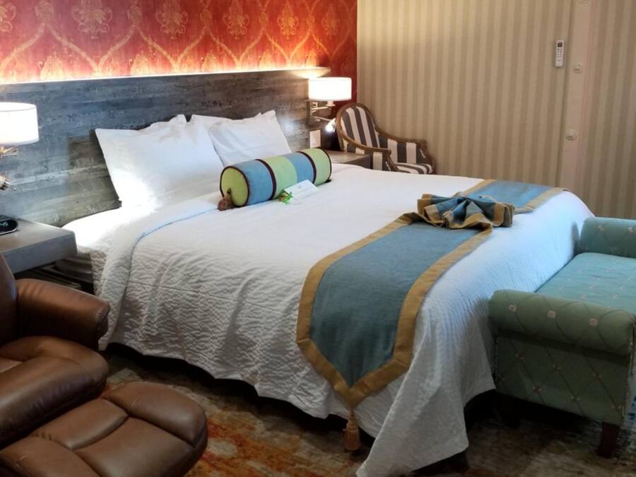 A hotel room with a large bed, a headboard, a desk with a lamp, a chair, a small table, and a striped curtain.