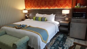Habitación de hotel con una cama grande, una mesita de noche, un aparador y una zona de estar con un banco.