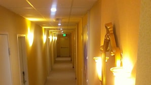 Un pasillo de hotel con varias puertas, apliques en la pared y un banco.