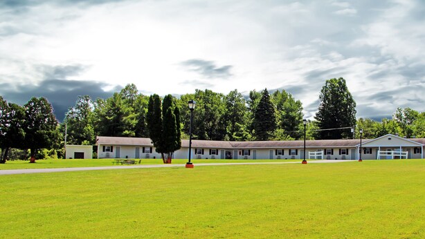 A motel with a large lawn, a covered parking area, and a row of single-story buildings with a flat roof.