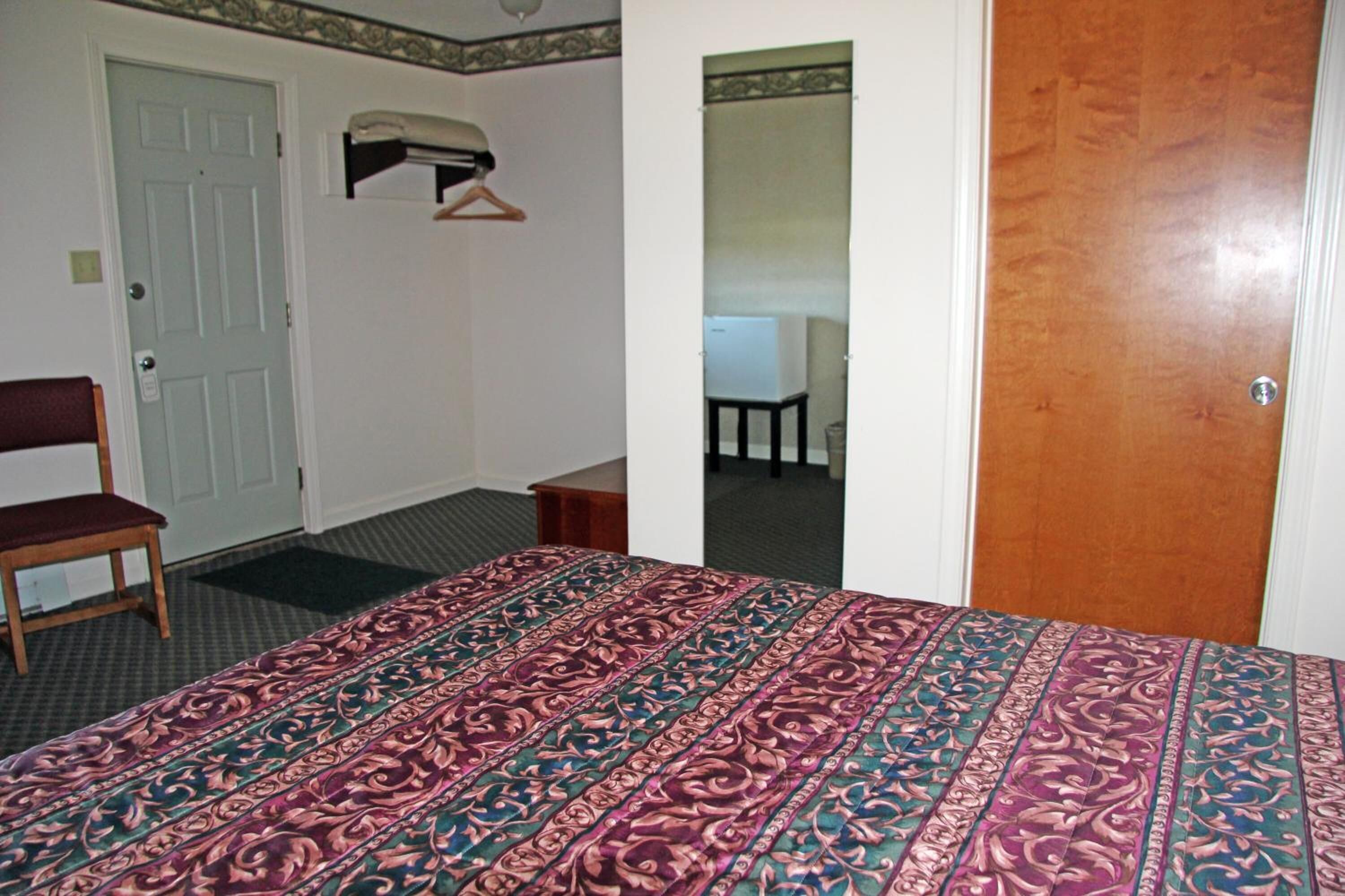 A hotel room with a bed, a chair, a desk, and a door.
