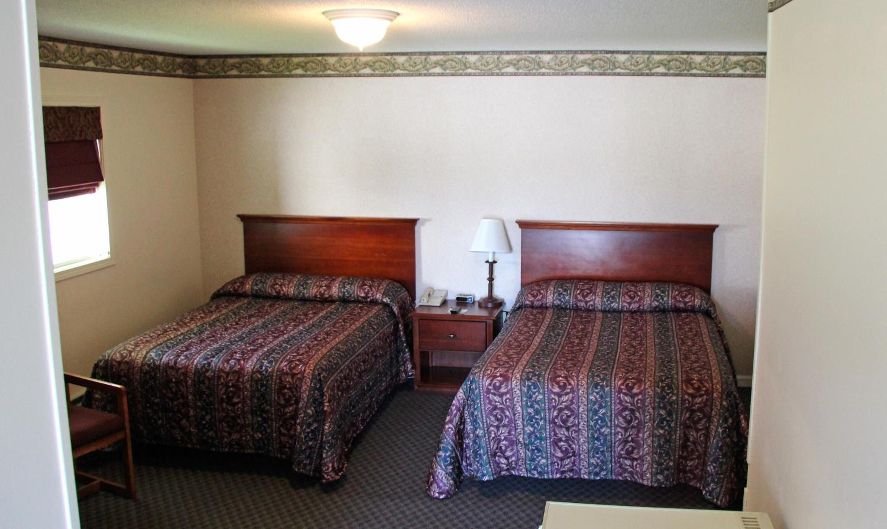 Une chambre d’hôtel avec deux lits simples, une table de chevet avec une lampe, un téléphone et une chaise.