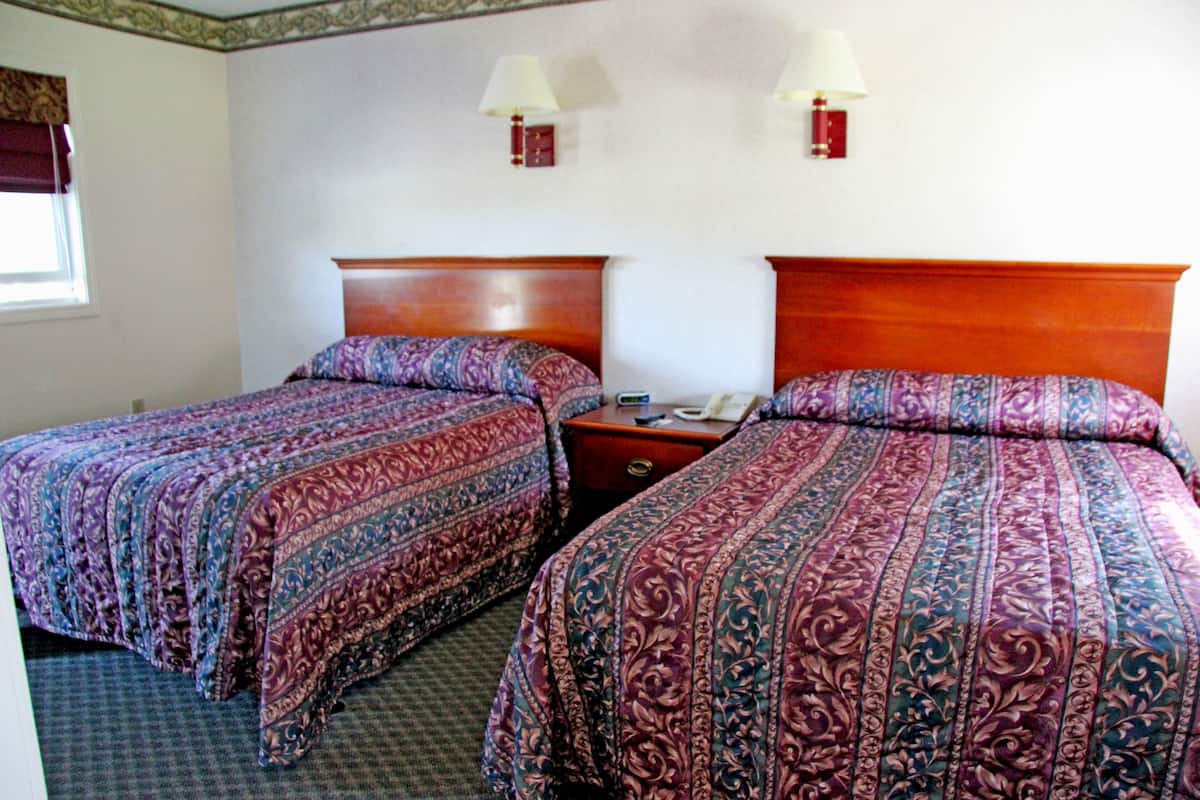Une chambre d’hôtel avec deux lits, chacun agrémenté d’une couvre-lit à motifs, d’une tête de lit en bois, de lampes de chevet et d’une table de chevet avec un téléphone.