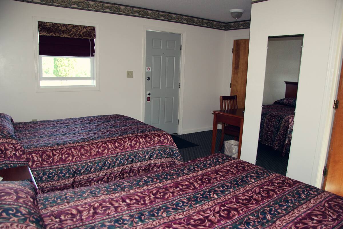 Une chambre avec deux lits, une fenêtre ornée d’un rideau foncé, une porte et un miroir.