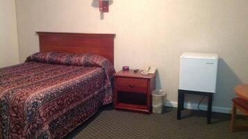 A hotel room with a bed, a nightstand with a lamp, a telephone, and a small refrigerator.